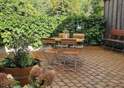 Gemütlicher Außenbereich mit Gartenmobiliar, bunter Pflanzen und Begrünung, ideal zum Entspannen im Grünen. Perfekte Location im Zentrum von zur Zitadelle für Veranstaltungen oder Kaffee im Freien.