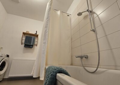 Duschbadewanne im stilvollen Badezimmer mit moderner Ausstattung und Waschmaschine, perfekt für Komfort und Entspannung in der Unterkunft zur Zitadelle.