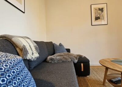 Gemütliches Wohnzimmer mit schwarzem Sofa, dekorativen Kissen, einer Decke, Schaffell und einem Couchtisch mit Vase und Blume, ideal für entspannte Aufenthalte in der Zur-Zitadelle Unterkunft.
