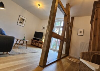 Gemütliches Wohnzimmer mit rustikalen Holzelementen, moderner Einrichtung, Fernseher und gemütlicher Atmosphäre – ideal für einen entspannten Aufenthalt im Ferienhaus zur Zitadelle.